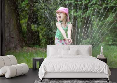 Happy toddler girl playing in a sprinkler on a hot summer day Wall mural