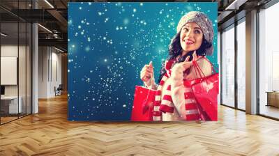 Happy young woman holding shopping bags in a snowy night Wall mural