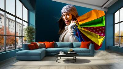 Happy young woman holding shopping bags on a dark blue background Wall mural