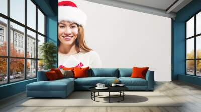 Happy young woman with Santa hat holding a Christmas present Wall mural