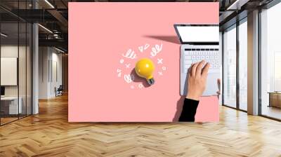 Person using a laptop computer and a light bulb - Flat lay Wall mural