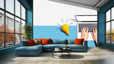 Person using a laptop computer and a light bulb - Flat lay Wall mural