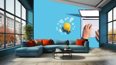 Person using a laptop computer and a light bulb - Flat lay Wall mural