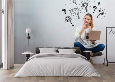 Question marks with young woman using her laptop on a grey background Wall mural