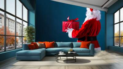 Santa holding a Christmas gift on a dark blue background Wall mural