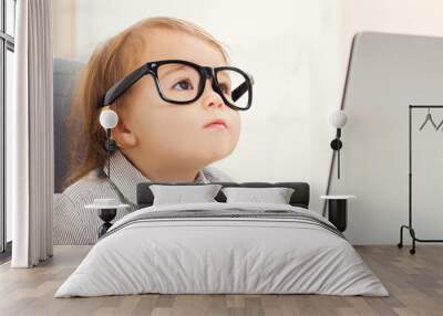 Smart toddler girl wearing big glasses while using her laptop Wall mural