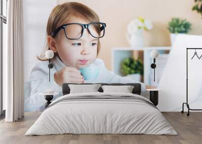 smart toddler girl with glasses drinking coffee while using a laptop Wall mural