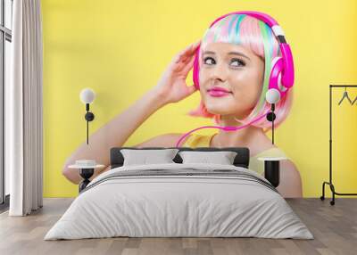 Woman in a colorful wig with headphones listening to music on a yellow background Wall mural