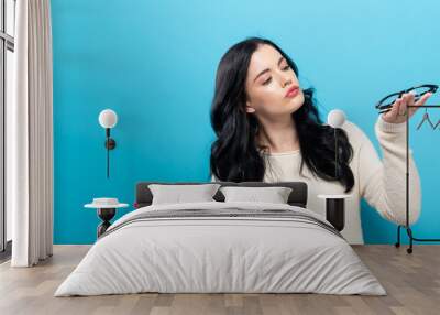 Young woman comparing two eye glasses on a blue background Wall mural