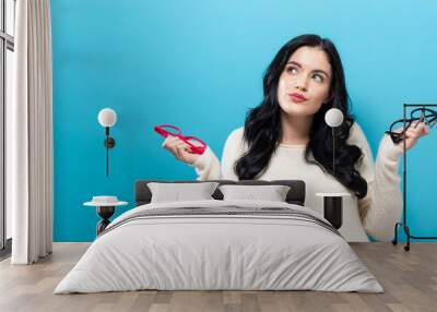 Young woman comparing two eye glasses on a blue background Wall mural