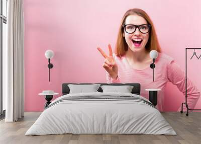 Young woman giving the peace sign on a solid background Wall mural