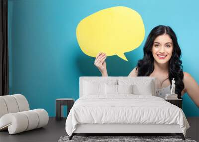 Young woman holding a speech bubble on a solid background Wall mural