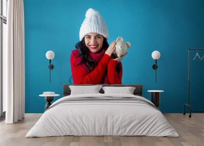 Young woman in winter clothes with a piggy bank on a dark blue background Wall mural