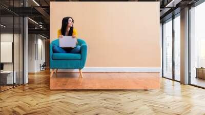 Young woman with a laptop computer in a thoughtful pose sitting in a chair Wall mural