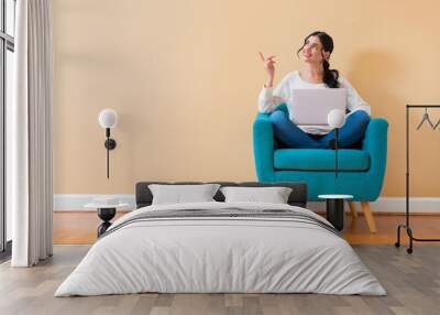 Young woman with a laptop computer pointing something sitting in a chair Wall mural