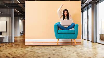 Young woman with a laptop computer with successful pose sitting in a chair Wall mural