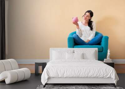 Young woman with a piggy bank sitting in a chair Wall mural