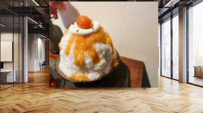 traditional Japanese sobert cold shaved ice dessert kakigori bingsu topped with orange marmalade sauce and fruit, oolong tea sauce on a black plate with white background and wooden table in summer Wall mural