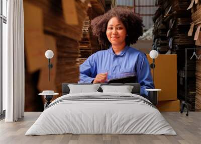 African American female delivery worker in safety uniform using a tablet to check shipment orders at parcels warehouse, paper manufacture factory for the packing industry, logistic transport service. Wall mural