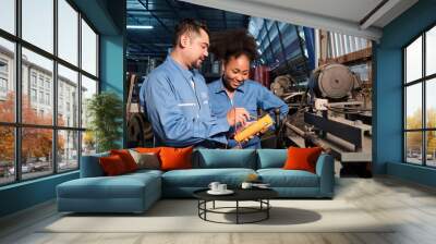 Asian male and female African American engineers in safety uniform work by inspecting machines' voltage current, checking, and maintaining at manufacture factory, electric system service occupations. Wall mural