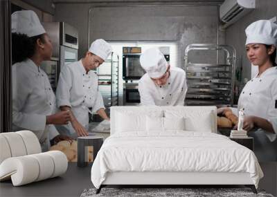 Multiracial professional gourmet team, four chefs in white cook uniforms and aprons knead pastry dough and flour, prepare bread, and bakery food, baking in oven at stainless steel restaurant kitchen. Wall mural