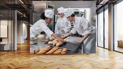 Professional gourmet team, three young chefs in white cook uniforms and aprons knead pastry dough and eggs, prepare bread, and fresh bakery food, baking in oven at stainless steel restaurant kitchen. Wall mural