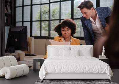 Young African American female worker sits, works with computer, brainstorming, talking, and discussing with Caucasian male colleague and partnership about business jobs in workspace office company. Wall mural