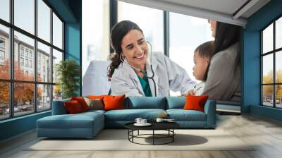 Young female pediatric doctor teases little Asian boy before medical examination at outpatient clinic hospital, people public health care checkups, and appointment visits. Wall mural