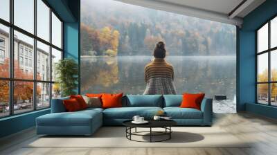 Woman sitting on a dock at a lake in autumn back view looking toward the forest and reflecting on the calm water of the lake during the fall season Wall mural