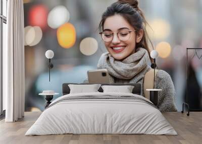 Young woman using a mobile phone while walking in the city, happily smiling and looking at her smartphone screen with glasses.  Wall mural