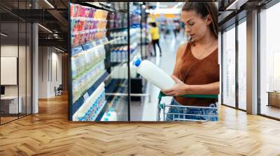 Female buying milk in supermarket stock photo. Young woman checking milk's labeling in supermarket Wall mural