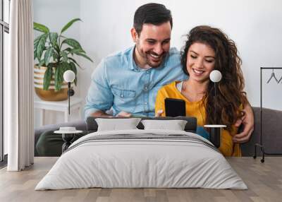 Happy smiling couple embracing and looking at smart phone at home stock photo Wall mural