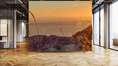 Sunset over mountain landscape. Sunset over Mountain Landscape. A stunning view of the sunset illuminating a mountain landscape, with tall grass and rocky formations in the foreground. Wall mural