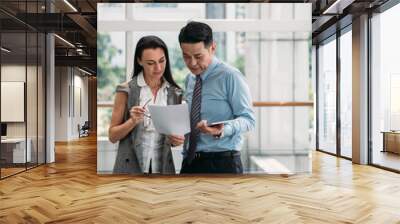 Two business people reading papers together in modern office with big windows.
Two serious business people standing and talking about documents in office lobby Wall mural