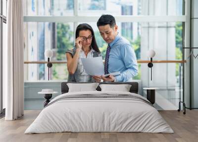 Two confident business people using a digital tablet and finance papers together while working in modern office with big window stock photo Wall mural