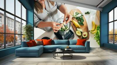 Woman is preparing a healthy detox drink in a blender - a  green smoothie with fresh fruits, green spinach and avocado. Healthy eating concept, ingredients for smoothies on the table, top view Wall mural