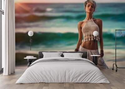 Young woman poses confidently on a beach at sunset, wearing casual attire with the ocean waves in the background, creating a serene and stylish summer vacation vibe. Wall mural