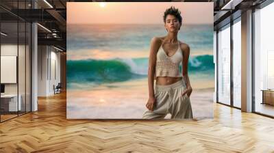 Young woman poses confidently on a beach at sunset, wearing casual attire with the ocean waves in the background, creating a serene and stylish summer vacation vibe. Wall mural