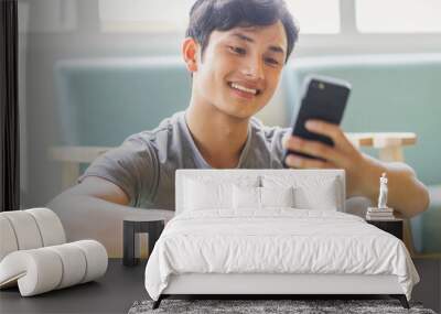 Asian man resting and using phone after exercising Wall mural