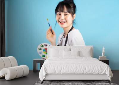 Beautiful Asian female painter holding quill pen and color palette on blue background Wall mural