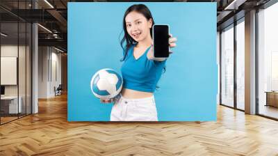 Beautiful Asian woman posing with soccer ball on blue background Wall mural