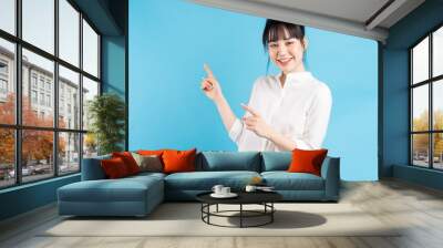 Beautiful Asian woman standing pointing on blue background Wall mural