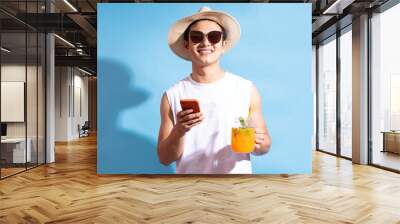 Handsome asian man wearing sunglasses holding cocktail in hand and using phone Wall mural