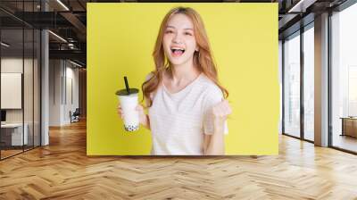 Image of young Asian girl drinking milk tea on yellow background Wall mural