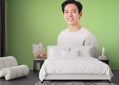 Image of young Asian man holding piggy bank on background Wall mural