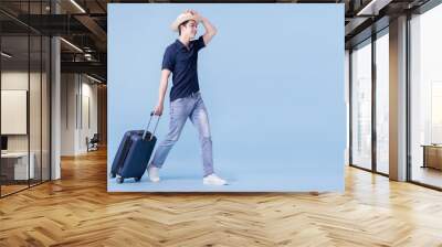 Image of young Asian man holding suitcase on blue background, travel concept Wall mural