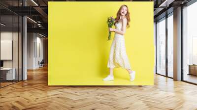 Image of young Asian woman holding flowers on yellow background Wall mural