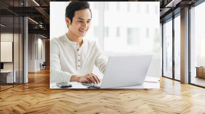 Portrait of male employee working on computer with happy expression Wall mural