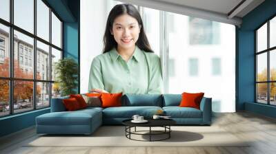 Portrait of young Asian businesswoman standing by the glass door with cheerful expression Wall mural