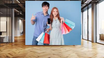 Young Asian couple carrying shopping bag on blue background Wall mural